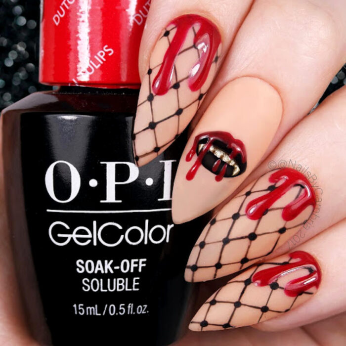 Manos con uñas largas y puntiagudas, pintadas en esmalte nude mate, con diseño de red y labios negros con colmillos de vampiro