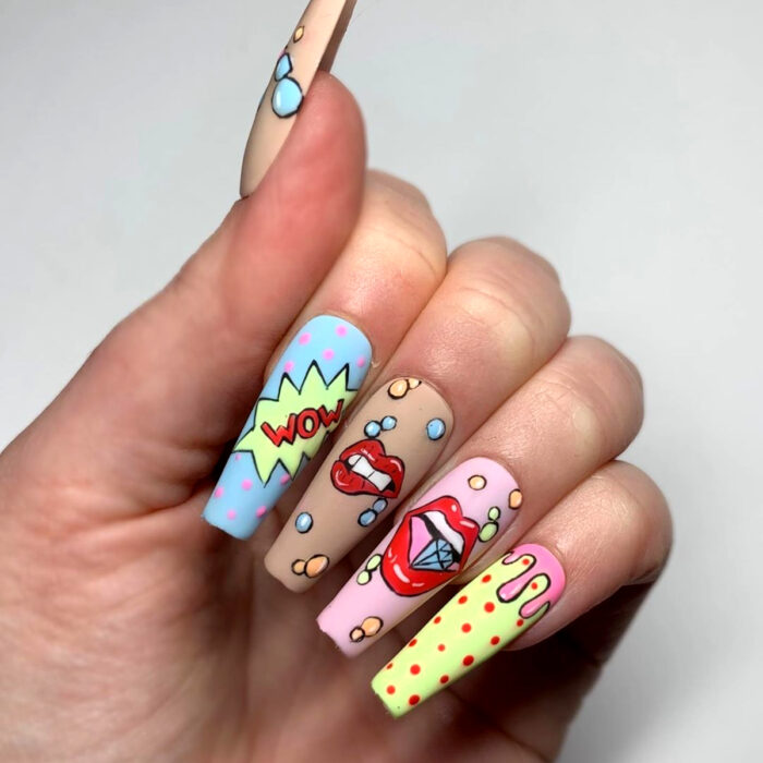 Manos con uñas largas cuadradas de bailarina, pintadas con esmaltes coloridos, con diseño de cómic y labios mordiendo diamantes