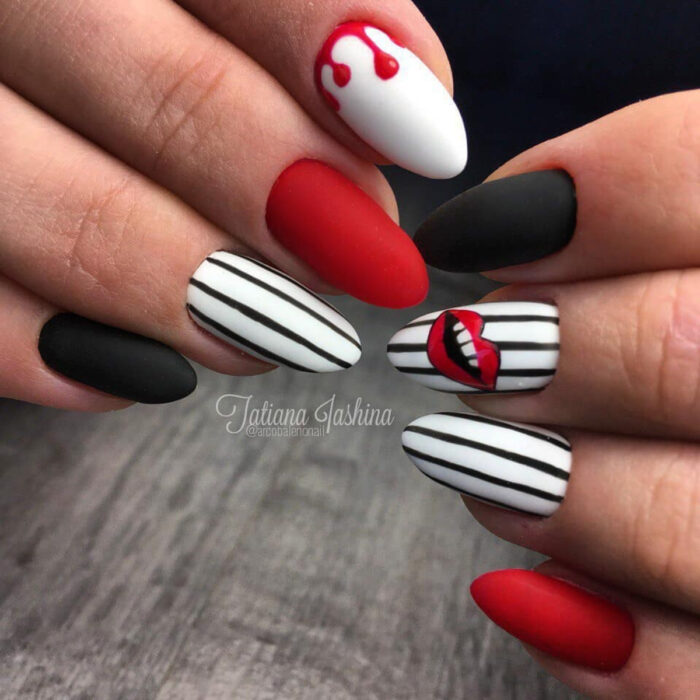 Manos de mujer con uñas largas en forma de almendra pintadas en esmalte mate blanco, rojo y negro, con diseños de rayas y labios sonriendo