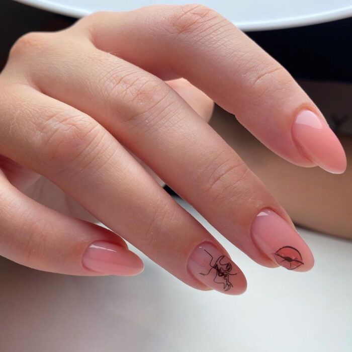 Manos de mujer con uñas largas en forma de almendra, pintadas en esmalte rosa nude, con diseño de labios y personas dándose un beso