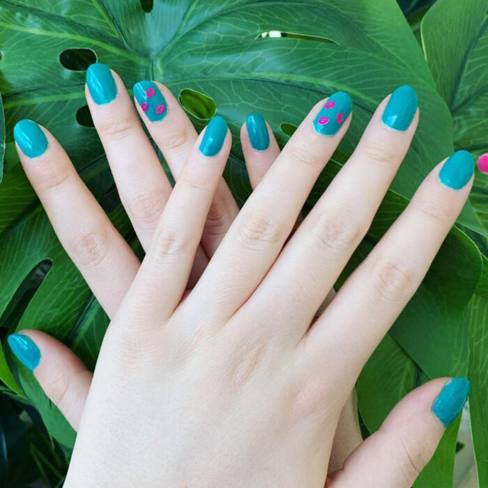 Manos de mujer con uñas cortas redondas, pintadas en azul con stickers de labios rosas