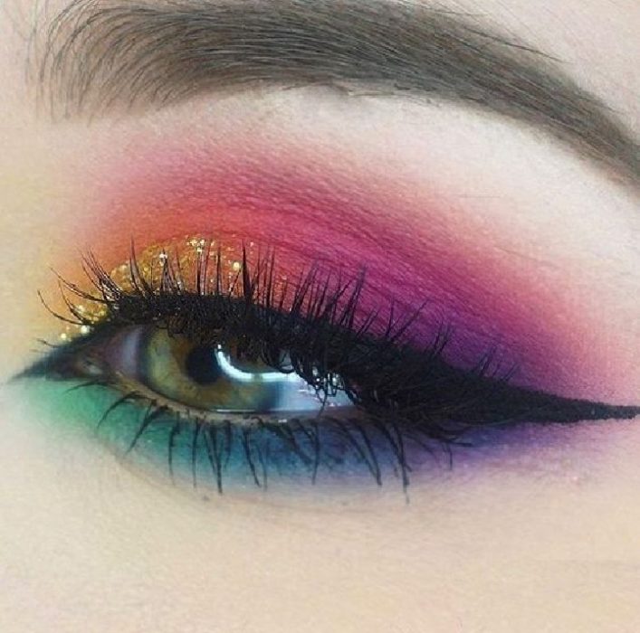 Maquillaje de arcoíris en colores azul, morado, amarillo, naranja, rosa con glitter dorado y delineador en negro estilo cat eye