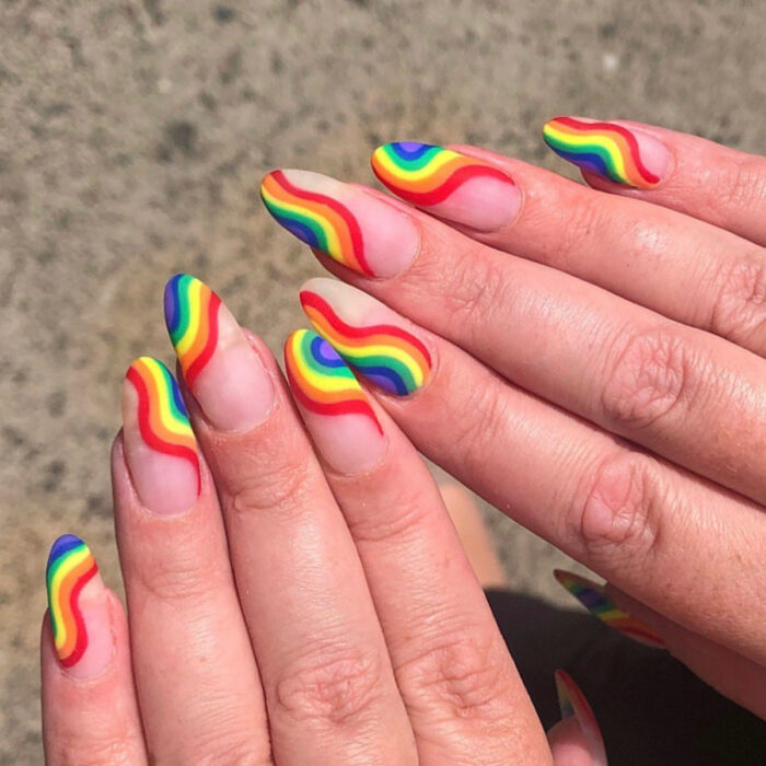 Diseños bonitos de manicura coloridos; manos de mujer con uñas largas en forma de almendra pintadas con esmalte nude de base y diseño psicodélico de arcoíris, colores rojo, anaranjado, amarillo, verde, azul y morado