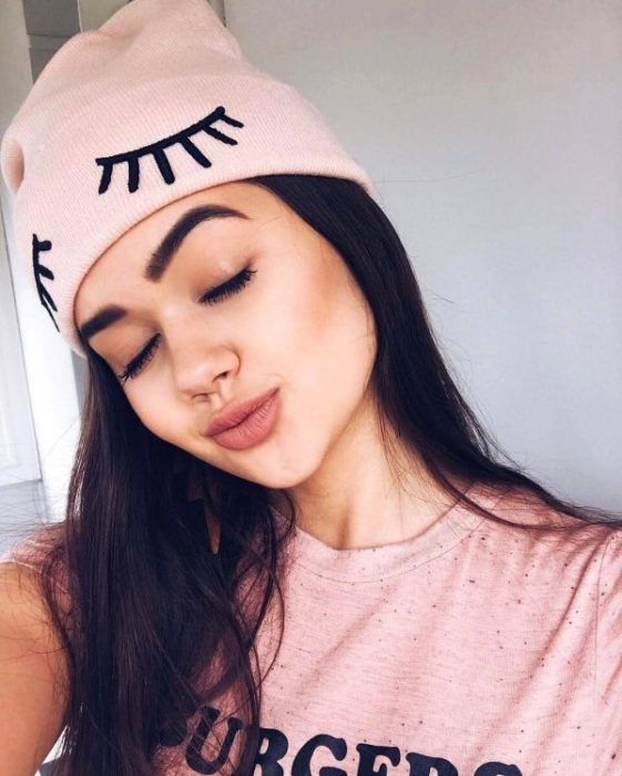 Chica llevando gorro tejido en color rosa palo con bordado de pestañas; ideas para llevar gorros y sombreros en otoño