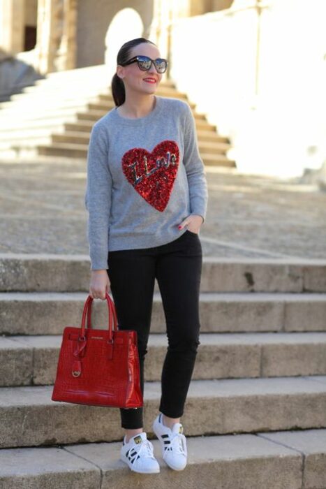 Chica usando jeans de color negro con suéter de color gris y un bolso de color rojo