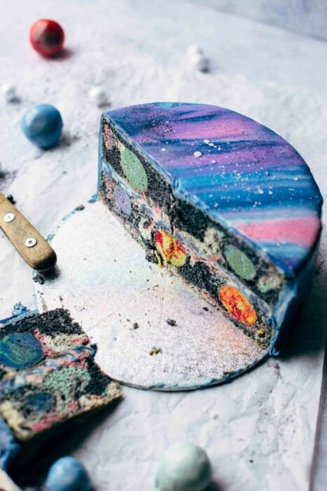 Pastel partido a la mitad, decorado con glaseado en tonos rosas y morados; Pasteles inspirados en la galaxia