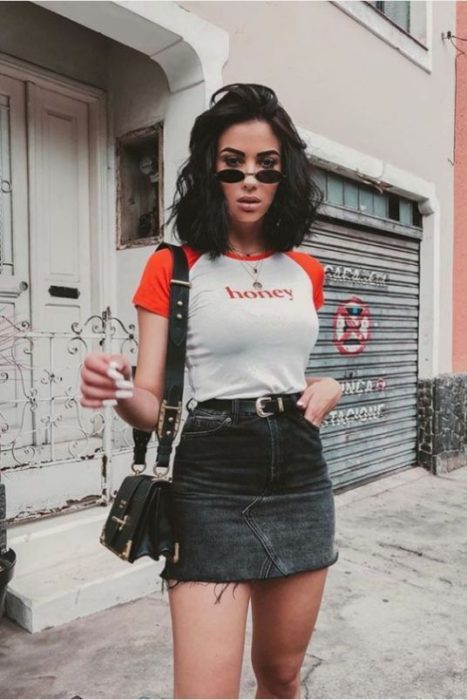 Chica morena de cabello corto con blusa gris de mangas rojas y falda negra de mezclilla