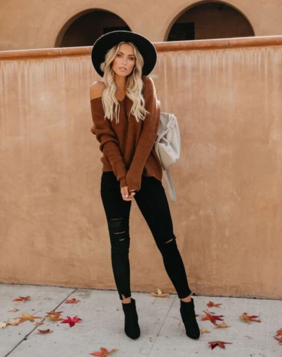 Chica usando sombrero negro, jeans, botines negros, suéter camel y bolso blanco