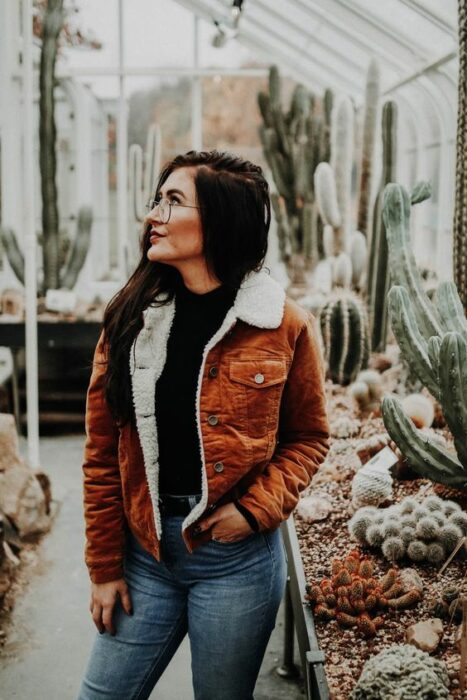 Chica usando jeans, suéter negro y chaqueta color caki con peluchito por dentro