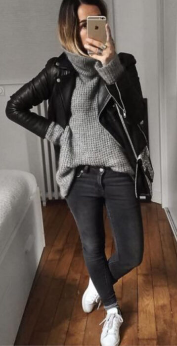 Chica usando jeans negros deslavados, tenis blancos, suéter gris holgado y chaqueta negra de cuero
