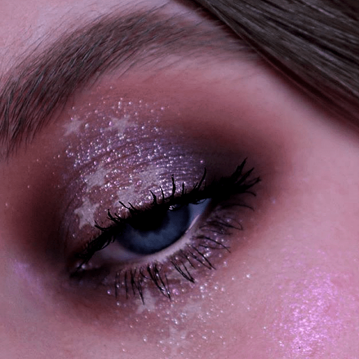 maquillaje de ojos con sombras metálicas, moradas y guindas, glitter rosa y formas de estrellas