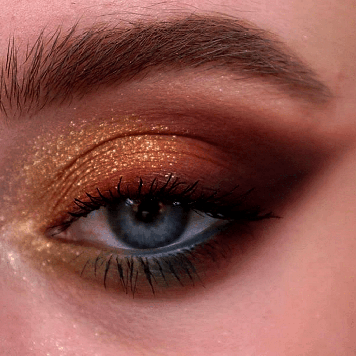 maquillaje de ojos con sombras doradas, cafés, amarillas, verdes, azules y guindas, con glitter dorado