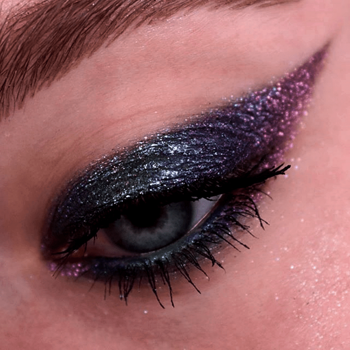 maquillaje de ojos con sombras azules, moradas, verdes y turquesa con glitter rosa y azul, y rímel negro