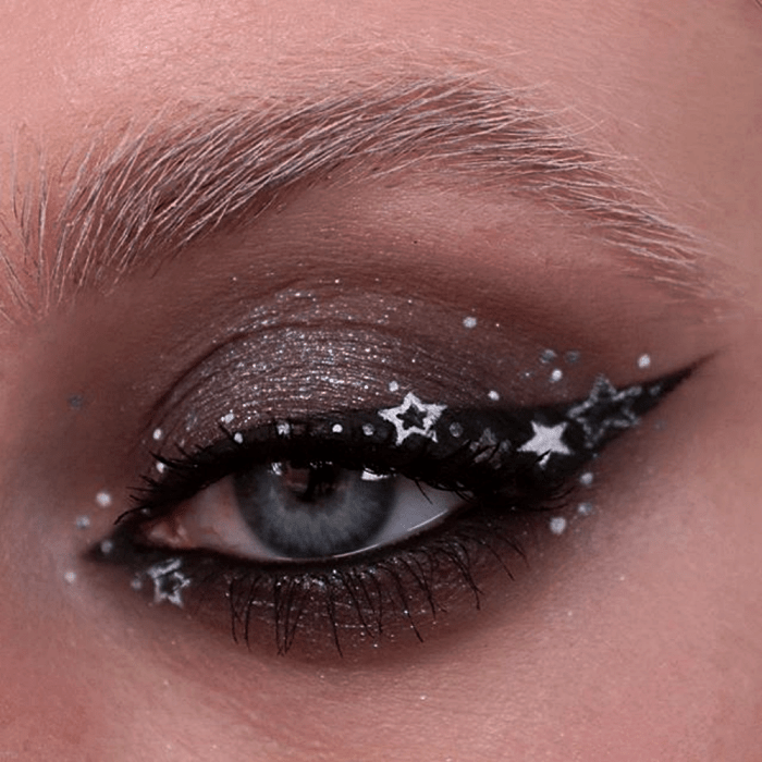 maquillaje de ojos con sombra gris, delineado negro cat-eye y delineado gráfico plateado en forma de estrellas