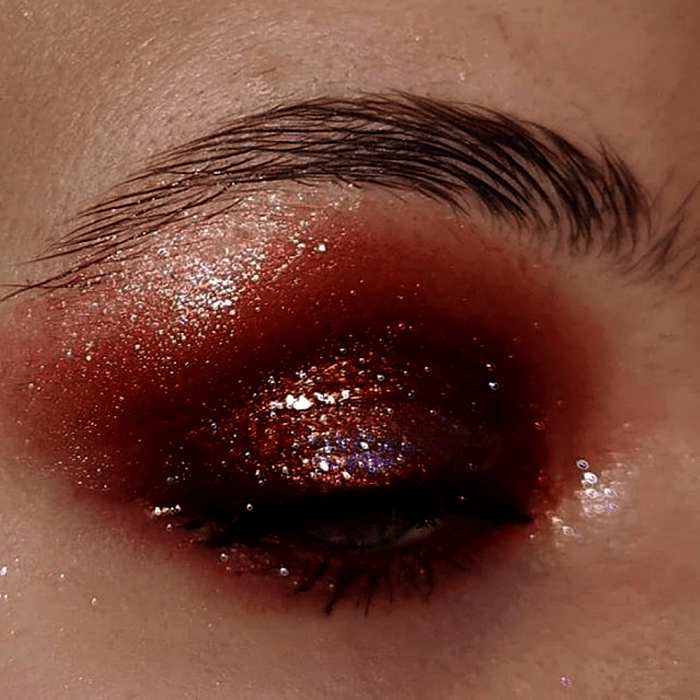 maquillaje de ojos con sombra estilo gloss color naranja, roja y guinda, con glitter multicolor y rímel negro