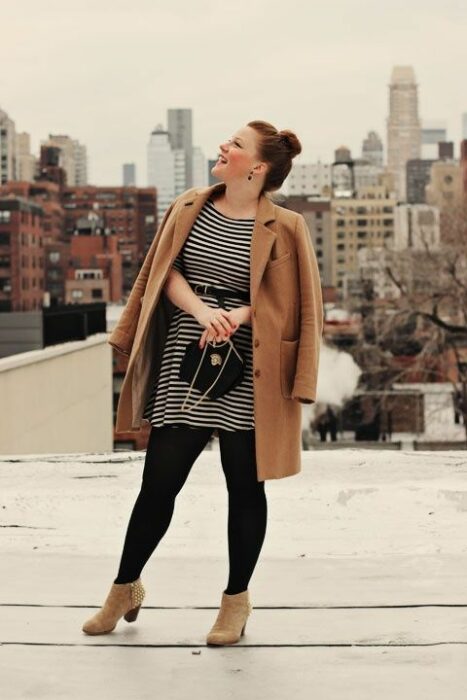 Chica curvy usando un abrigo de color café y un vestido de rayas abajo con botines de estoperoles