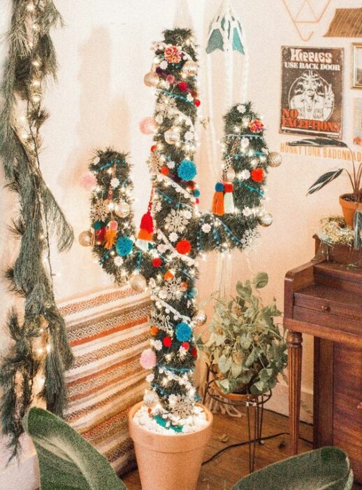 Árbol de navidad en forma de cactus en una sala blanca con un mueble de madera a un costado