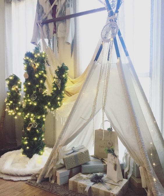 Árbol de navidad en forma de cactus con luces amarillas decorando una habitación con paredes y cortinas blancas cerca de un tepee blanco