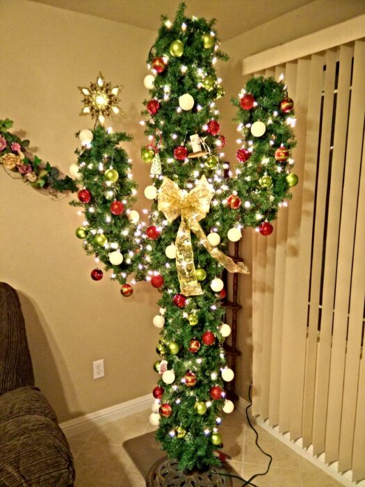 Árbol de navidad en forma de cactus en una sala blanca decorado con luces amarillas, esferas rojas y un gran moño dorado