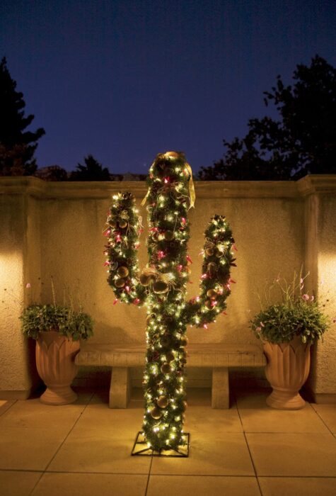 Árbol de navidad en forma de cactus ubicado fuera de la casa, decorado con luces amarillas y esferas rojas