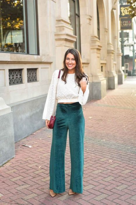 Mujer con cabello oscuro suelto, blusa blanca y pantalón verde esmeralda