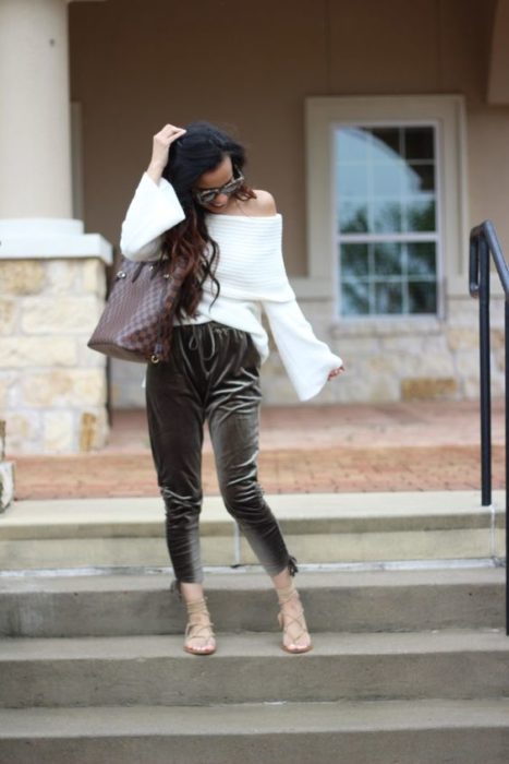 Mujer morena de cabello largo con blusa sin hombros en blanco y pantalón gris de terciopelo