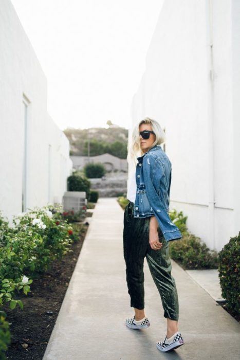 Chica rubia fotografiada de espaldas, llevando blusa blanca, chaqueta de mezclilla y pantalón verde de terciopelo