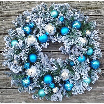 Corona blanca de Navidad con esferas azules y plateadas colgando en muro de madera