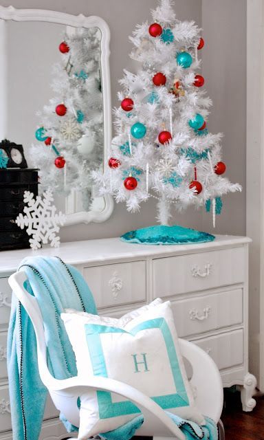 Mueble blanco con un arbolito de Navidad blanco decorado con esferas rojas y azules, con un espejo de fondo