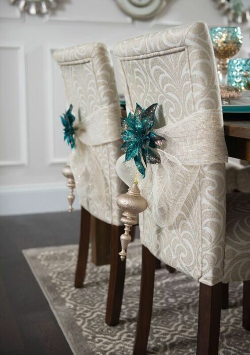 Sillas blancas con patas cafés decoradas con listón blanco y estrellas azul turquesa en la parte trasera, además de una esfera dorada colgante
