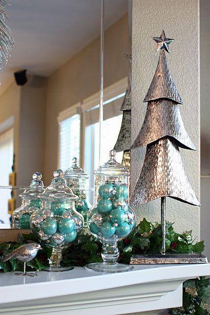 Muebles café con dos jarrones transparentes llenos de esferas turquesas, un pino navideño de metal a un lado y un espejo detrás