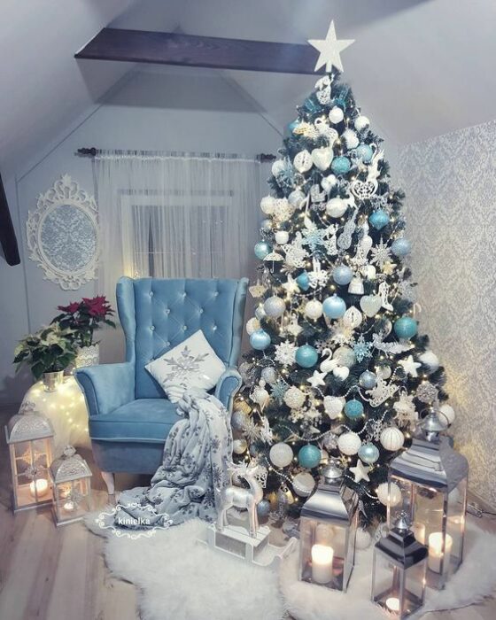Árbol de Navidad verde con esferas turquesas y blancas al lado de un sillón azul en una habitación con paredes blancas