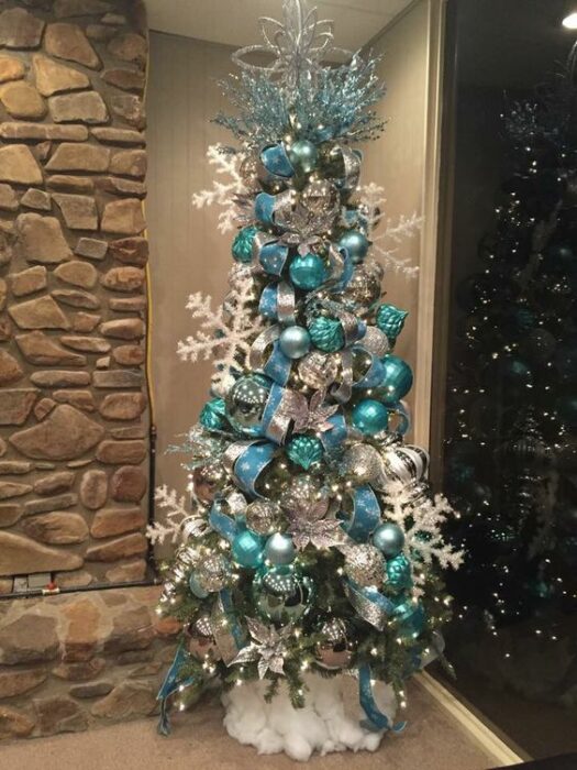 Árbol de Navidad blanco con grandes copos blancos y grandes esferas azul Tiffany en una habitación con pared de piedra
