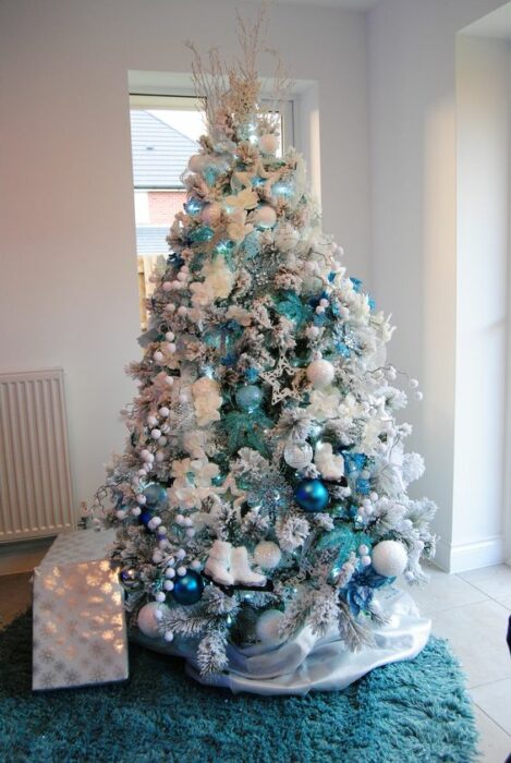 Árbol navideño blanco decorado con esferas azules aqua y turquesa en una habitación blanca
