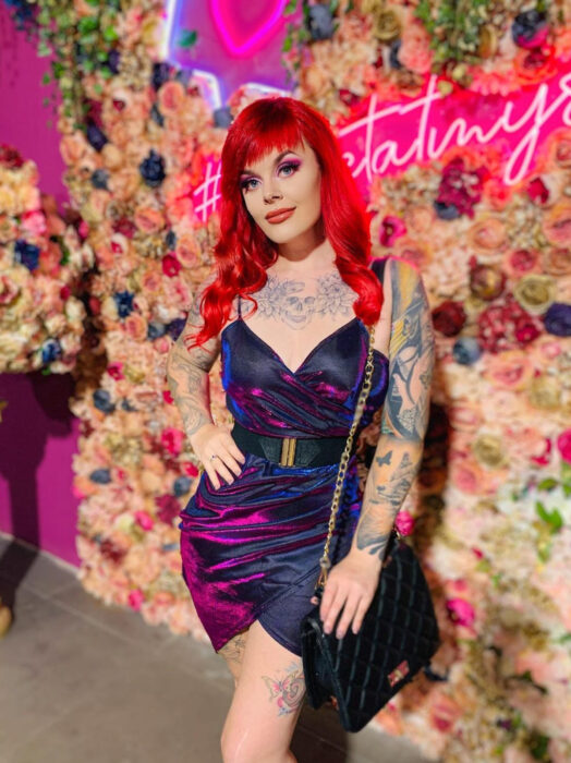 Vestido iridiscente, holográfico de tirantes con cinto ancho, mujer pelirroja con tatuajes de calavera y flores en pecho y brazos