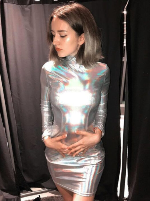 Vestido iridiscente, holográfico con cuello y mangas, mujer de cabello corto y castaño claro