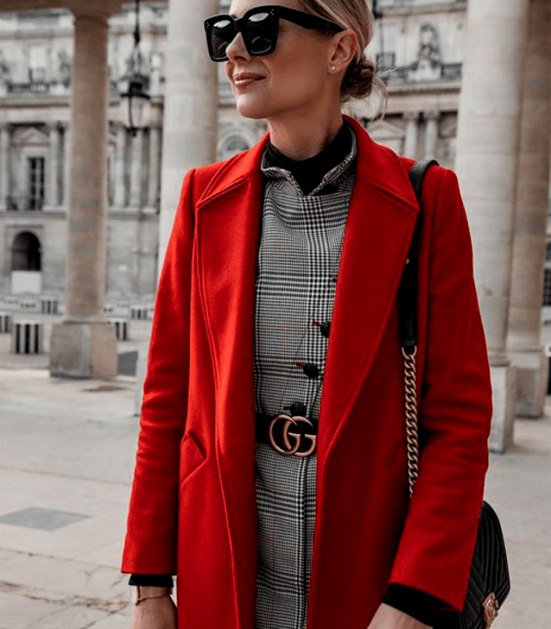 mujer rubia con abrigo largo rojo, vestido gris de cuadros, cinturón negro y bolso negro