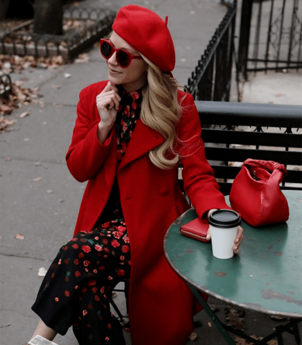 mujer rubia con abrigo rojo largo, vestido negro con flores rojas, y bolso rojo