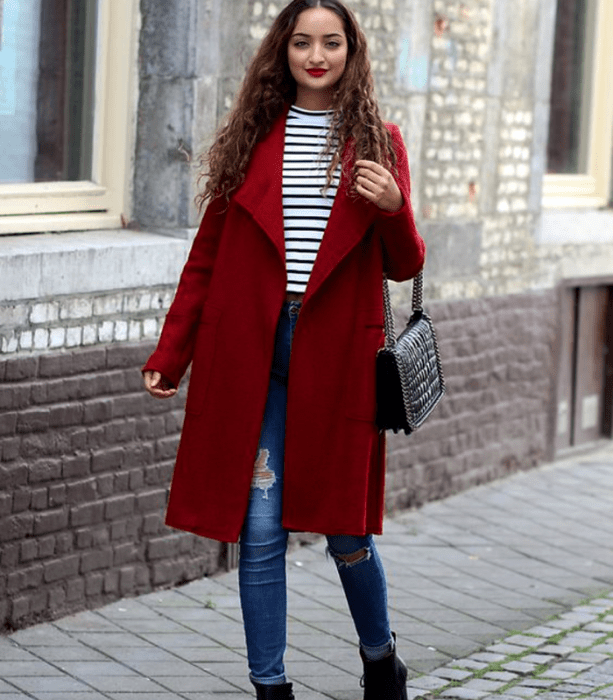 mujer con abrigo largo rojo, top blanco de rayas, jeans ajustados y botines negros