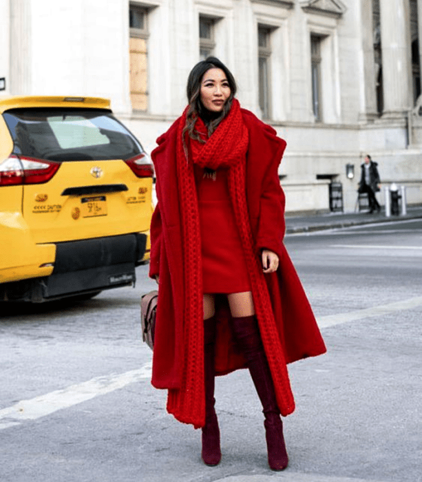 mujer de cabello castaño con abrigo rojo, vestido mini y botas largas guindas