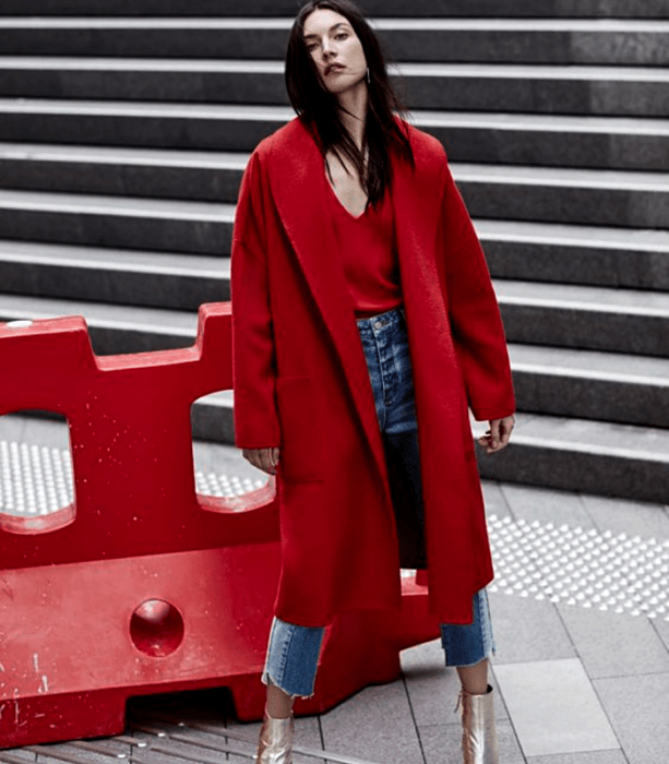 mujer de cabello negro con abrigo rojo, jeans ajustados y botines dorados