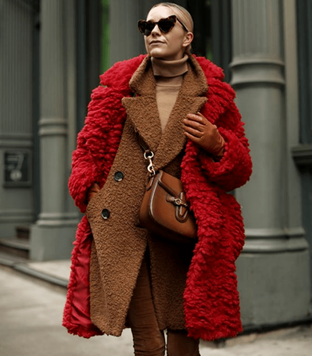 mujer rubia con suéter beige, abrigo rojo afelpado y bolso de piel café