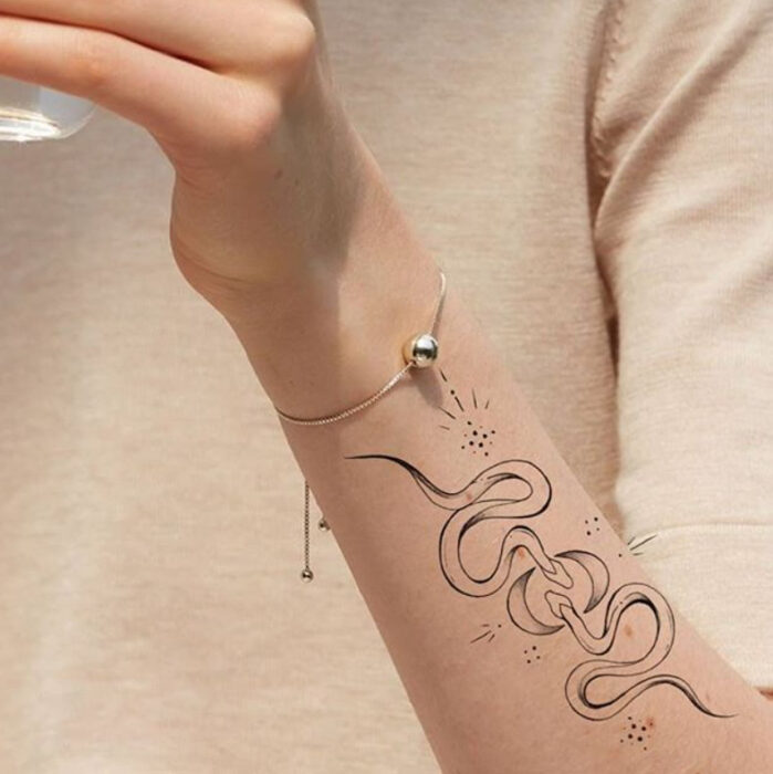 Tatuaje de la silueta de dos serpientes que se encuentran sobre la zona del antebrazo