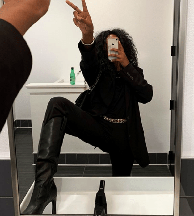 mujer morena usando una camiseta negra, saco negro, pantalones negros de vestir, botas de tacón negras y bolso negro