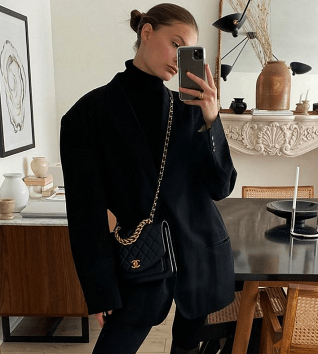mujer rubia, top negro de cuello alto, saco oversized negro, bolso negro de piel y leggings negros