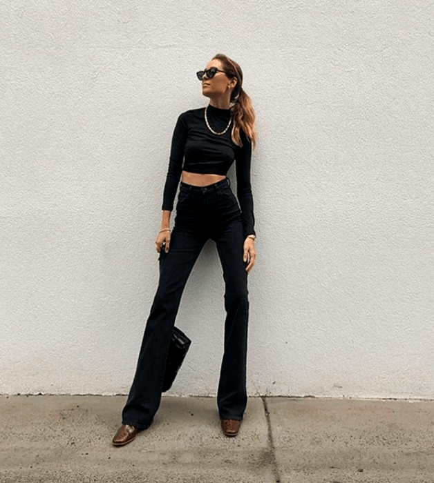 mujer rubia con lentes de sol, crop top negro de manga larga, high waist jeans negros y botines cafés de piel