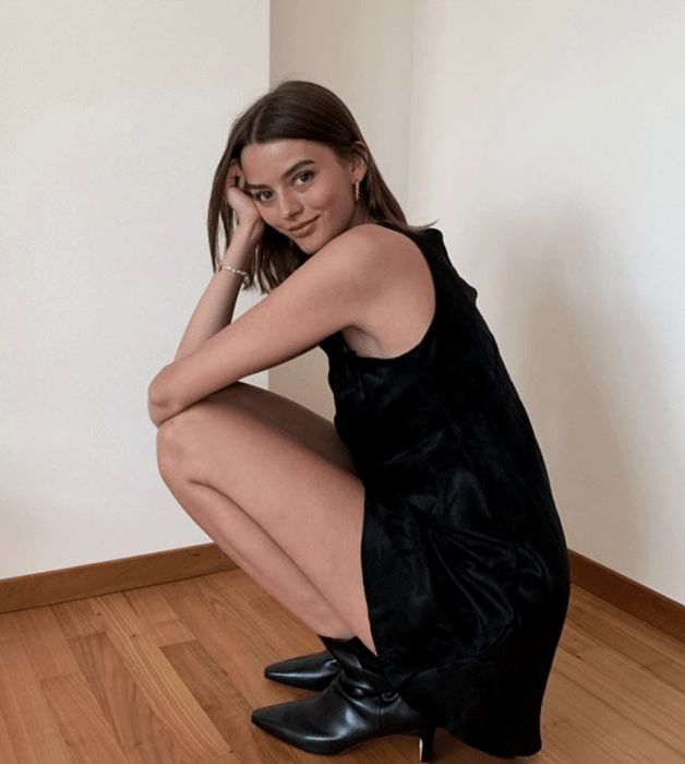 mujer de cabello castaño usando un vestido negro sin mangas, botines negros de cuero