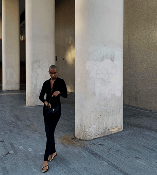 mujer morena usando un vestido largo negro con cuello en V y sandalias negras de piso y un bolso pequeño negro