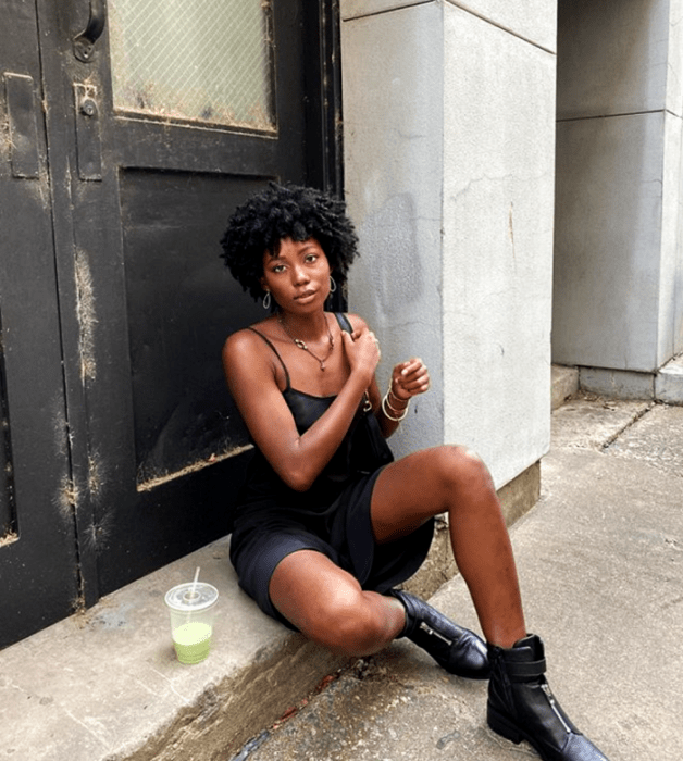 mujer morena usando un vestido midi negro de tirantes, bolso negro mini, y botines negros
