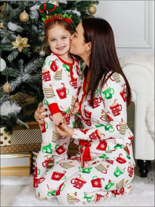 Mujer y niña usando la misma pijama, la mujer le besa la mejilla a la niña, con el árbol de navidad detrás de ambas